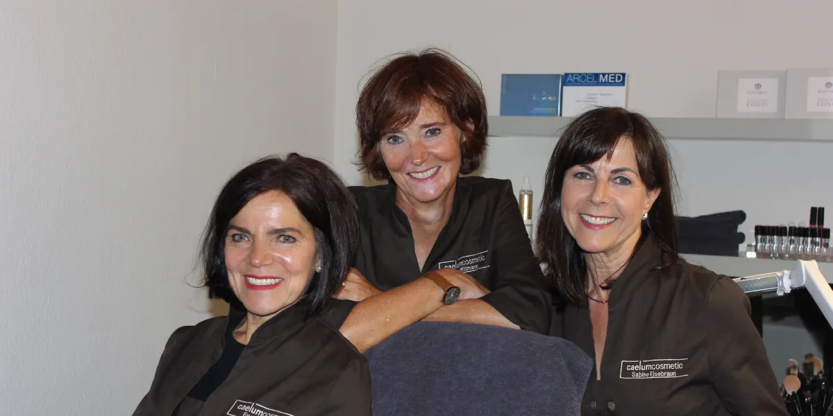 Drei Mitarbeiterinnen von Caelum Cosmetic in ihren dunklen Studiojacken, lachend im Studio